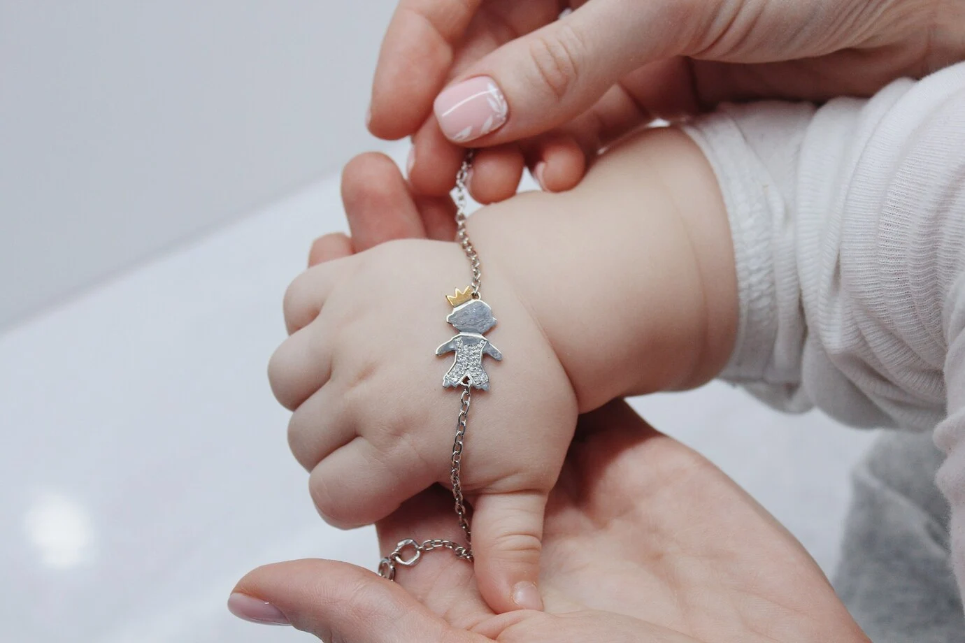 Жена държи ръката на бебе със сребърна гривна
