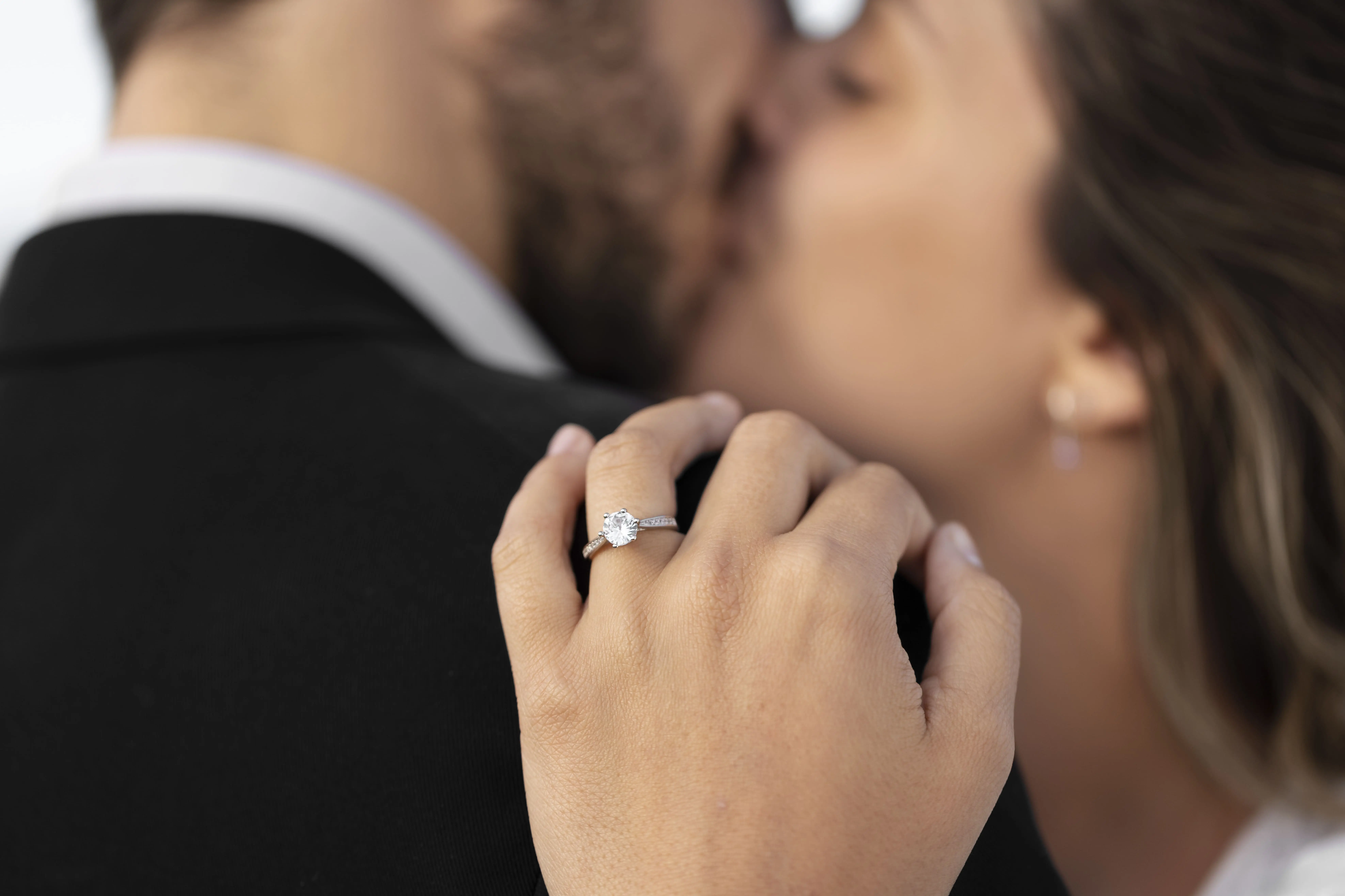 Woman and man in a kiss and engagement ring in the foreground