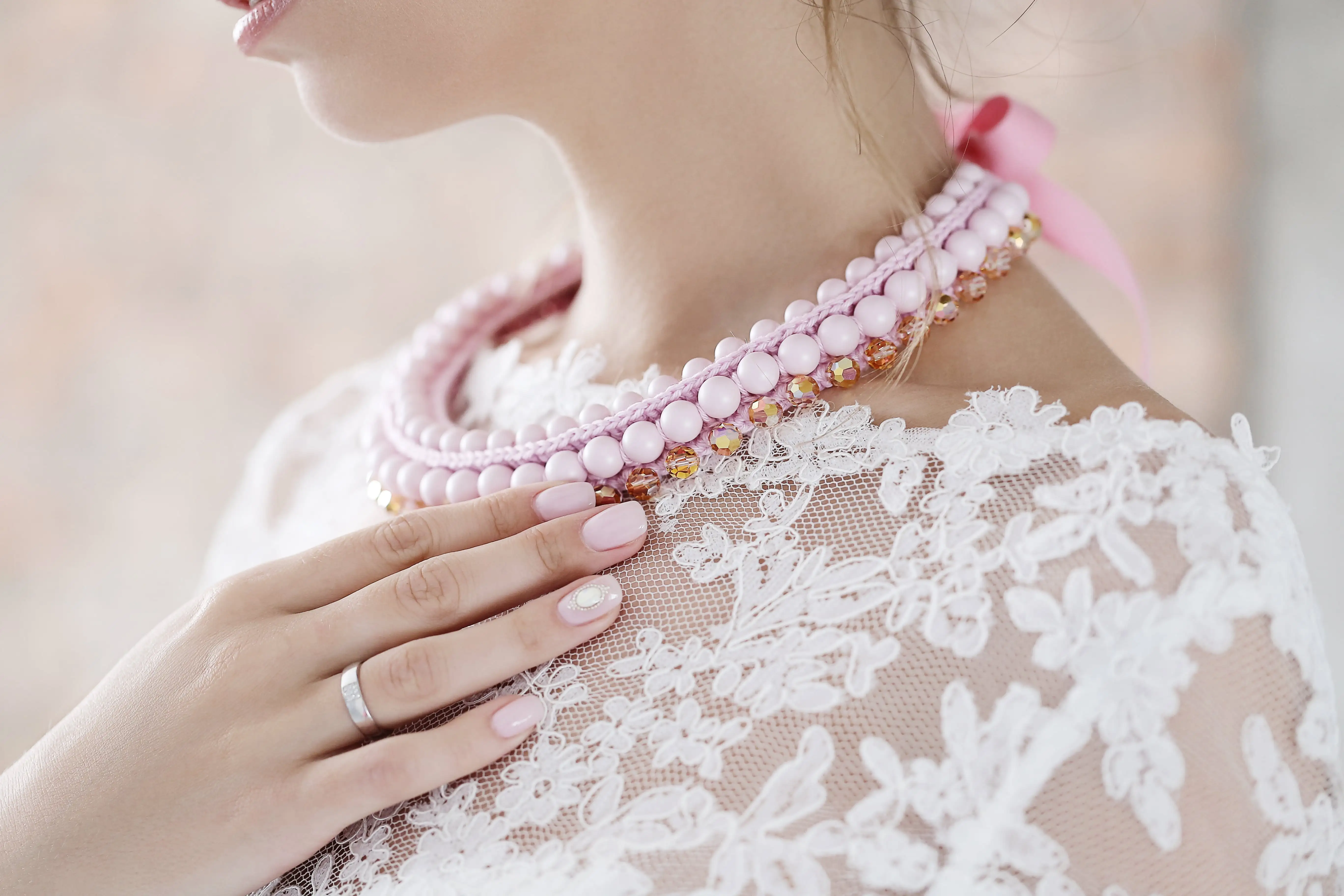 Růžový perlový náhrdelník na krku ženy v bílých šatech